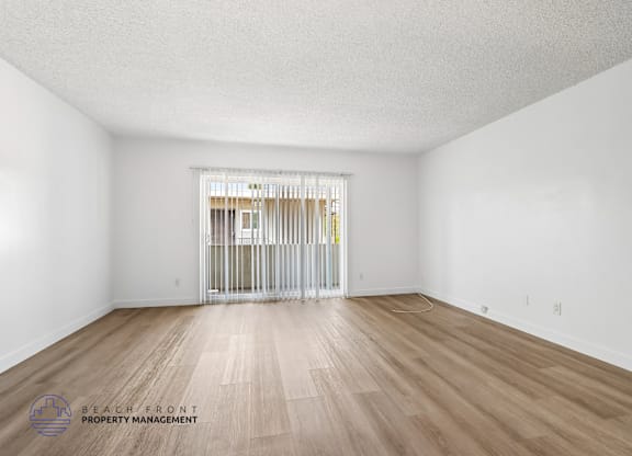 A room with wooden floors and white walls, with a doorway leading to another room.