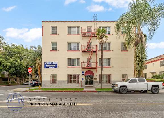 A white building with a sign that says "Now Leasing" in front of it.