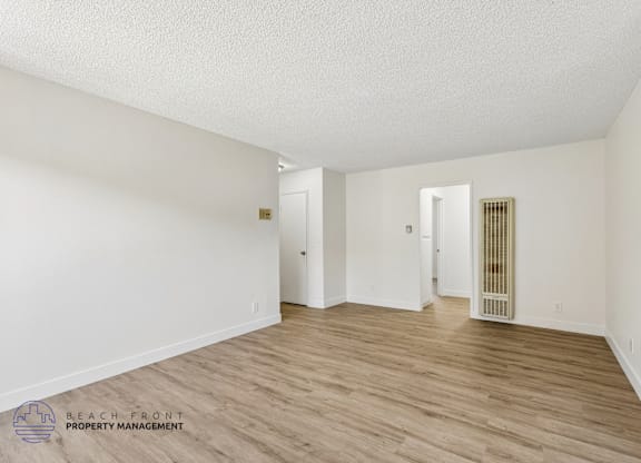 A spacious room with wooden flooring and white walls, with a door on the right side.