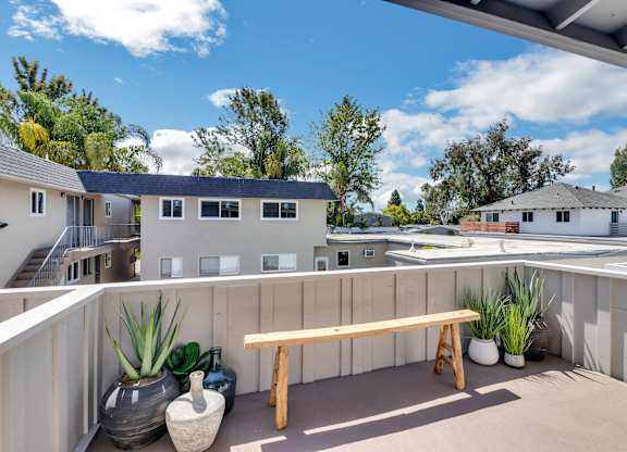 A wooden bench sits on a patio with a potted plant and vase beside it.