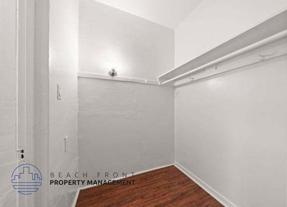A white room with a wooden floor and a white wall with a pipe running along it.