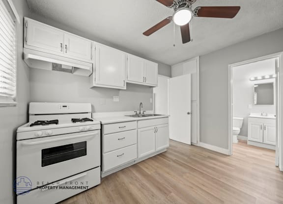 A white kitchen with a stove, sink, and cabinets.