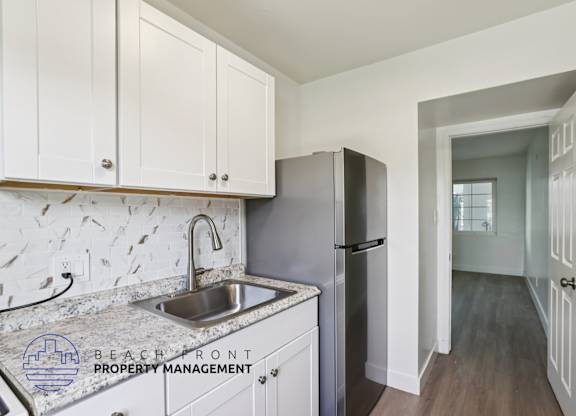 A kitchen with a sink and refrigerator with a logo for Beachfront Property Management.