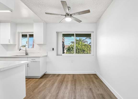 A white kitchen with a ceiling fan and a window.