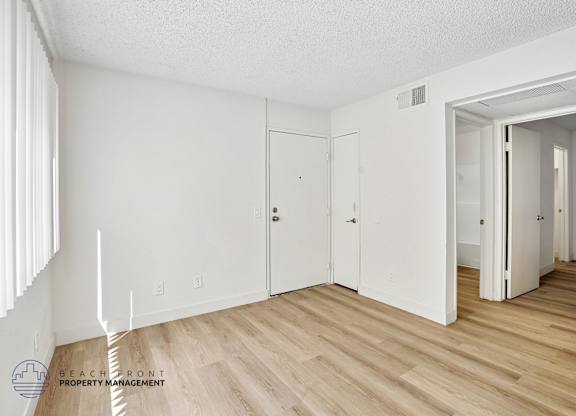 A white room with wooden floors and a logo for Beachfront Property Management in the bottom left corner.