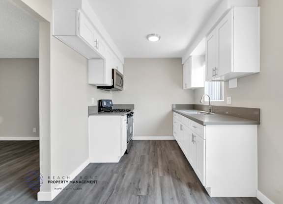 A kitchen with white cabinets and a wooden floor.
