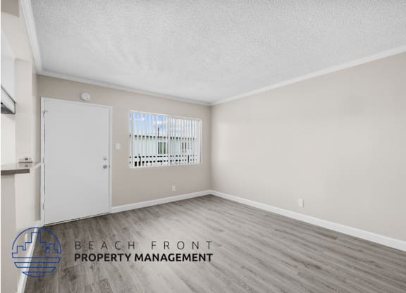 the spacious living room of an apartment with wood flooring and a door to the