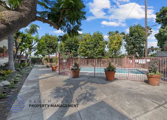 A pool surrounded by a fence and potted plants.