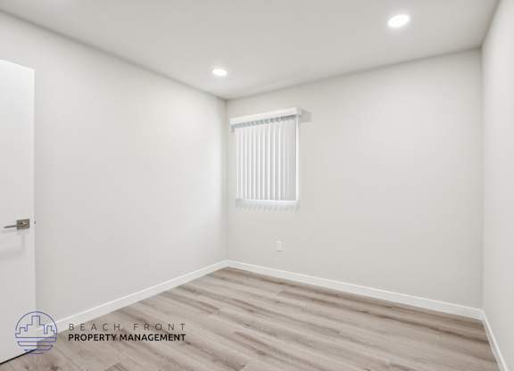A room with a wooden floor and a window with blinds.