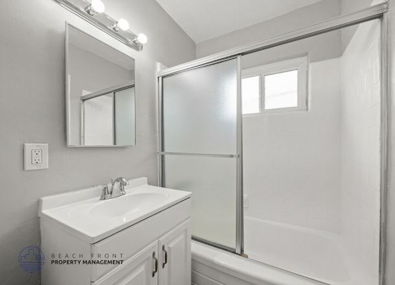 A white bathroom with a sink, mirror, and shower.