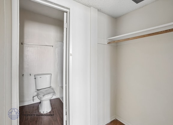 A white toilet is in a small bathroom with a wooden floor.
