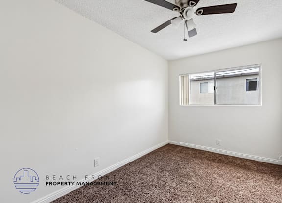 A room with a ceiling fan and a window with a view of a building outside.