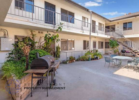 A courtyard with a BBQ grill and chairs is surrounded by apartment buildings.
