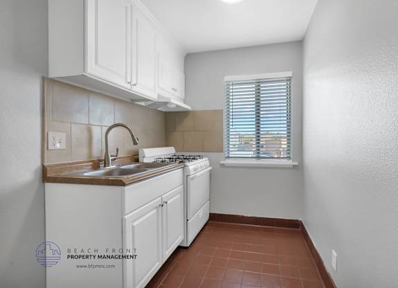A kitchen with white cabinets and a window with blinds.