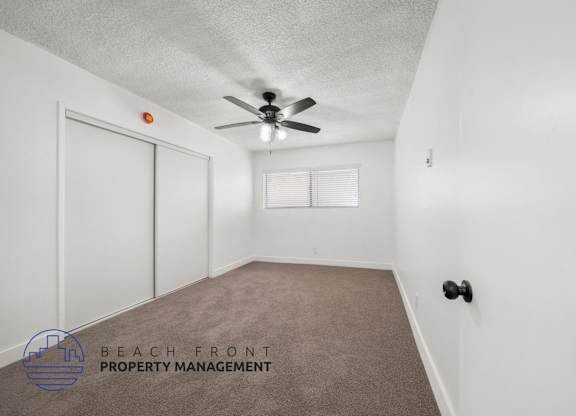 A room with a carpet floor, a ceiling fan, and a window with blinds.