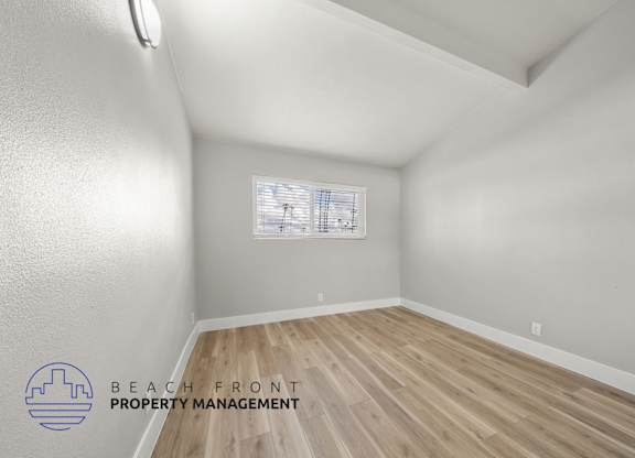 A room with wooden flooring and a window with blinds.