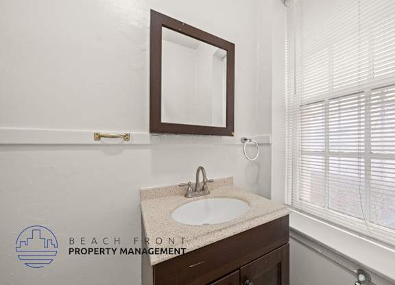 A bathroom with a sink, mirror, and window with blinds.