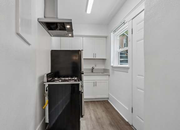 A black stove is in a white kitchen with wood floors.