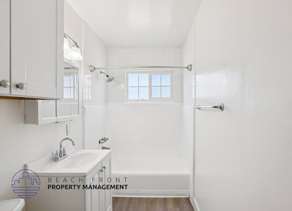 A white bathroom with a sink, mirror, and bathtub.