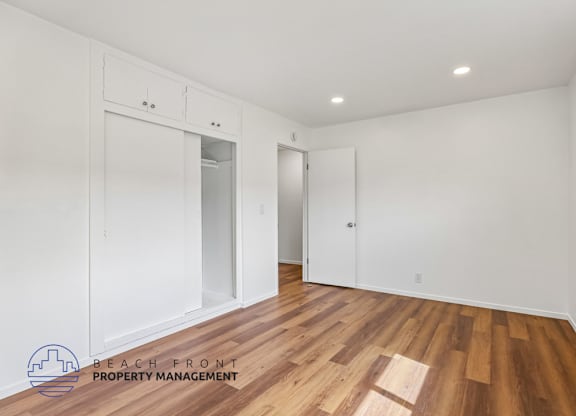 A room with wooden flooring and white walls, with a logo for Beach Front Property Management in the bottom left corner.