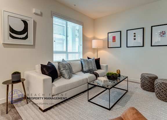 A living room with a white couch, a glass coffee table, and a window with blinds.