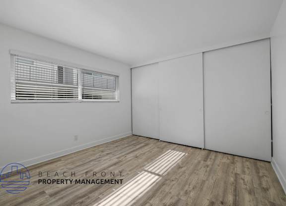 A room with a window and wooden flooring, with a logo for Beach Front Property Management.