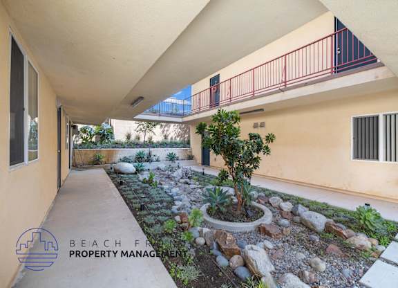 A balcony with a red railing overlooks a landscaped garden area.