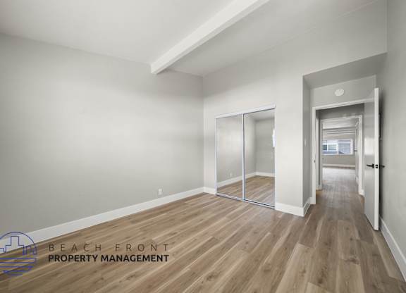 A spacious room with wooden flooring and a logo for Beach Front Property Management in the corner.