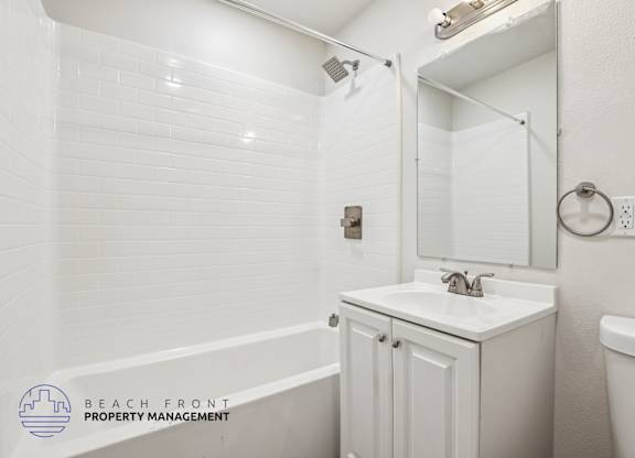 A white bathroom with a sink, mirror, and bathtub.
