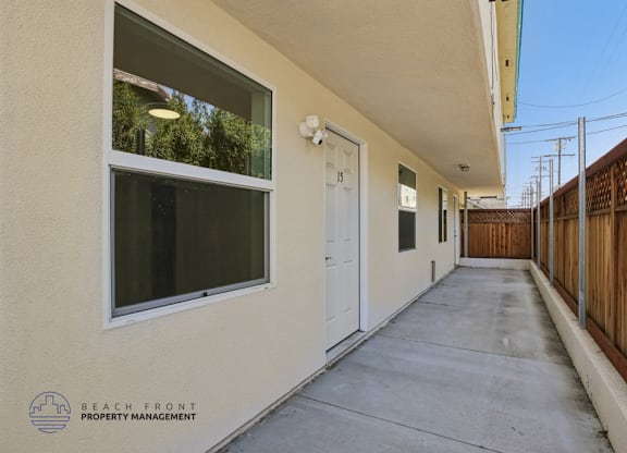 A long, narrow hallway with a white door and a window on the left side.