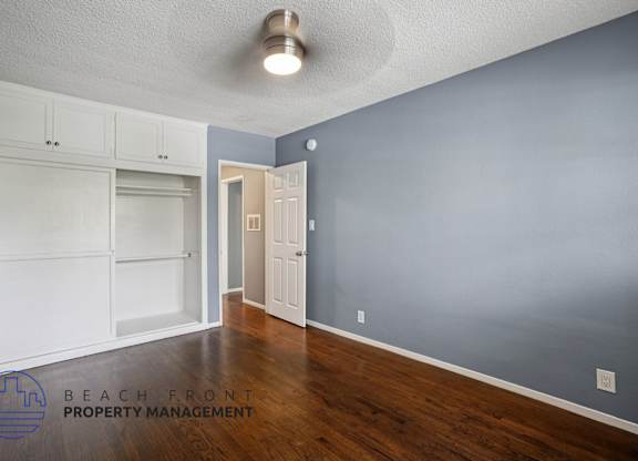 A room with a white ceiling, wooden floor, and a white door.