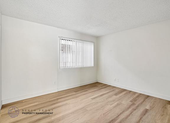 A room with wooden flooring and a window with blinds.