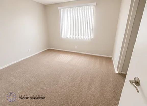 A carpeted room with a window and a door.