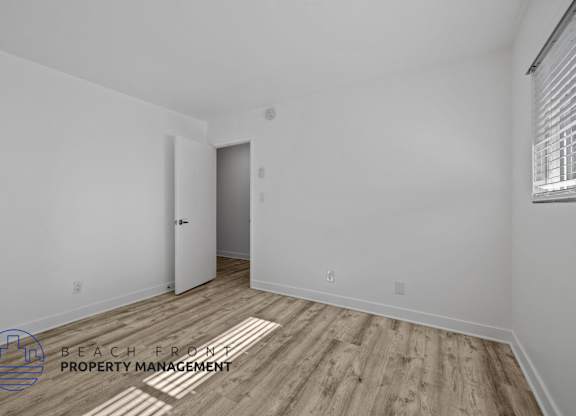 A room with a wooden floor and a door on the left side.