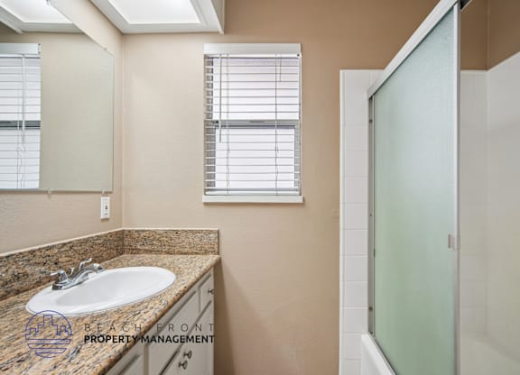 A bathroom with a sink, mirror, and shower.