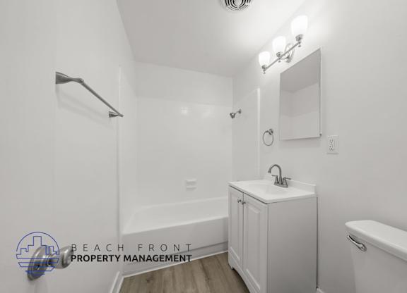 A white bathroom with a sink, mirror, and bathtub.