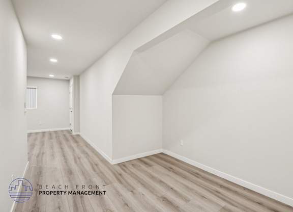 A spacious room with wooden flooring and white walls, managed by Beach Front Property Management.