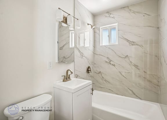A white bathroom with marble tiles and a tub.