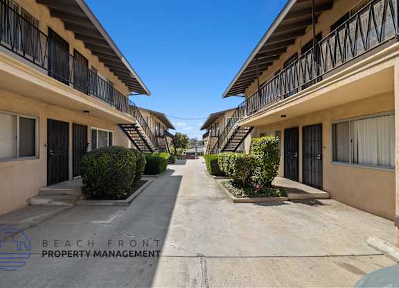 a long walkway between two buildings with balconies and bushes