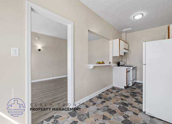 A kitchen with a white refrigerator and a stone floor.