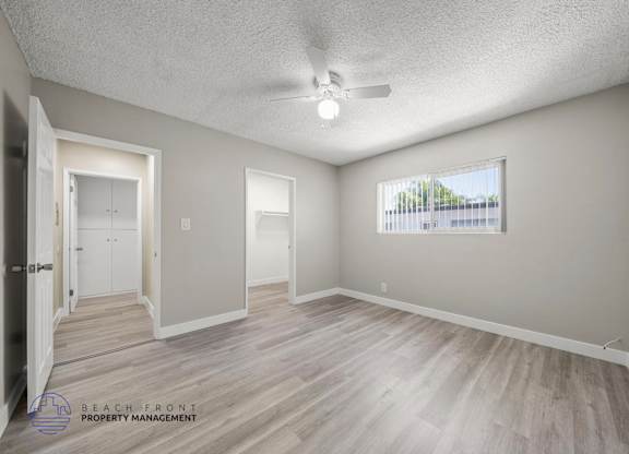 A spacious room with wooden flooring and a window overlooking a parking lot.