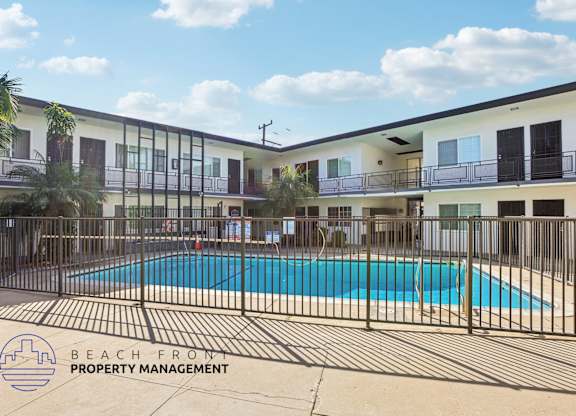 A pool surrounded by a fence and a building with balconies.