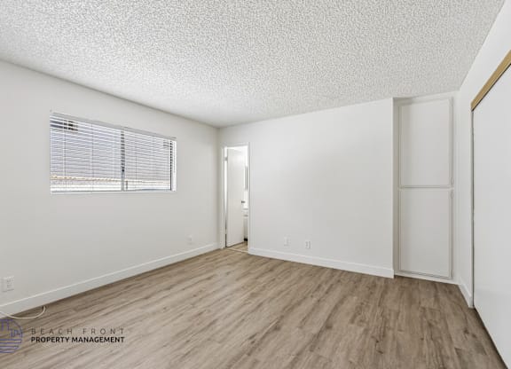 A spacious room with wooden flooring and a window with blinds.