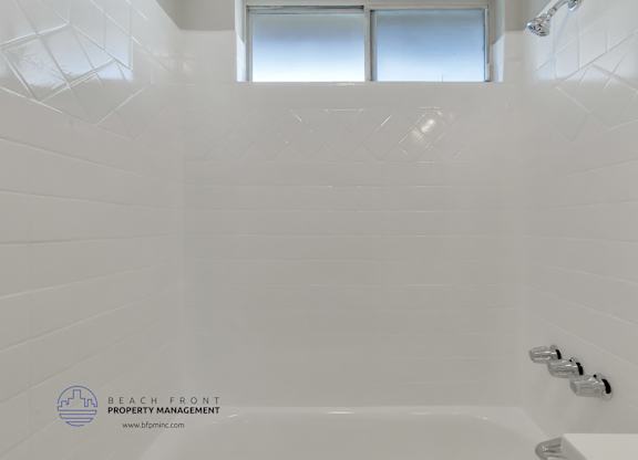A white bathroom with a tub and shower head.