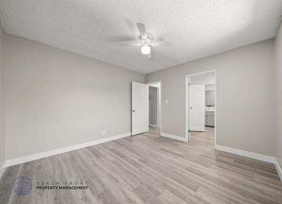 A spacious room with a ceiling fan and light, and a wooden floor.