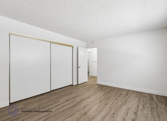 A room with white walls and wooden flooring, with a sliding door and a small white cabinet.