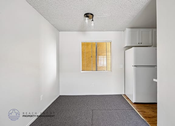 A room with a white refrigerator and a window with blinds.