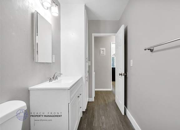 A white bathroom with a toilet, sink, mirror, and a wooden floor.