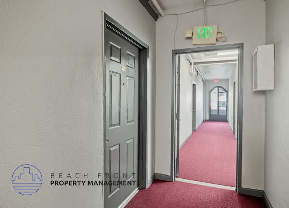 A hallway with a red carpet and a green exit sign.