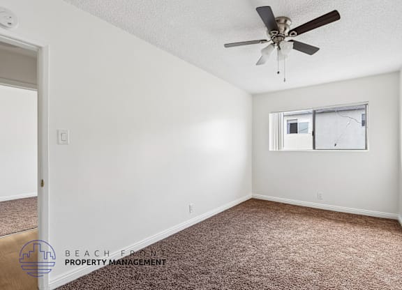 A room with a ceiling fan and a window with a screen door.